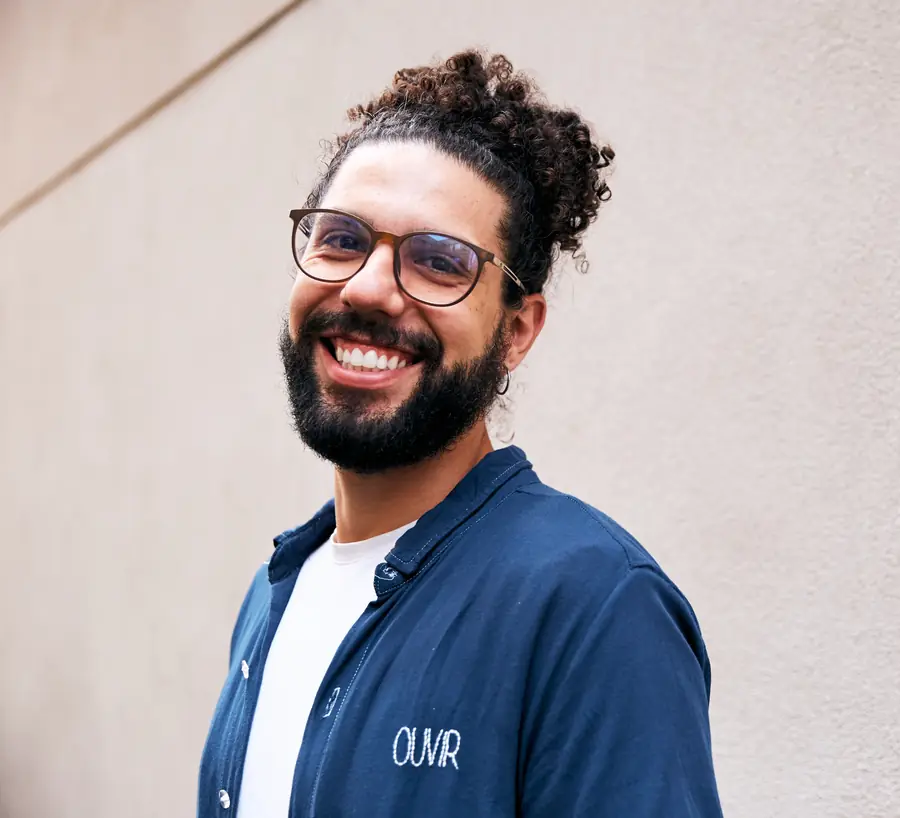 João Victor Morais, psicólogo, sorrindo, encostado em uma parede clara