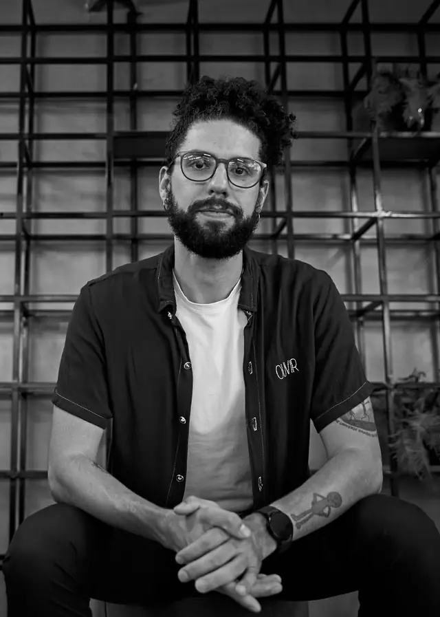 Retrato em preto e branco de João Victor Morais, psicólogo, sentado com as mãos entrelaçadas