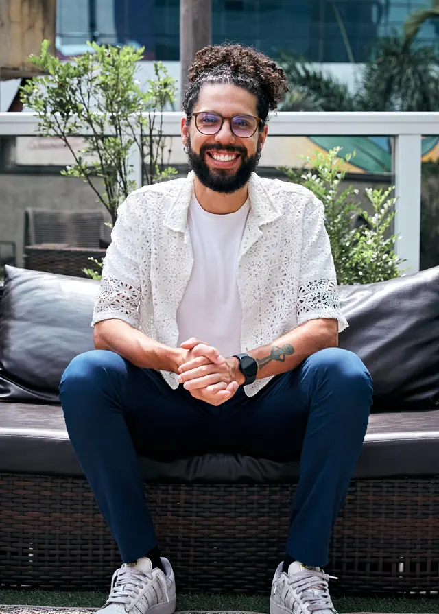 João Victor Morais sorrindo, sentado, com as mãos entrelaçadas sobre o colo