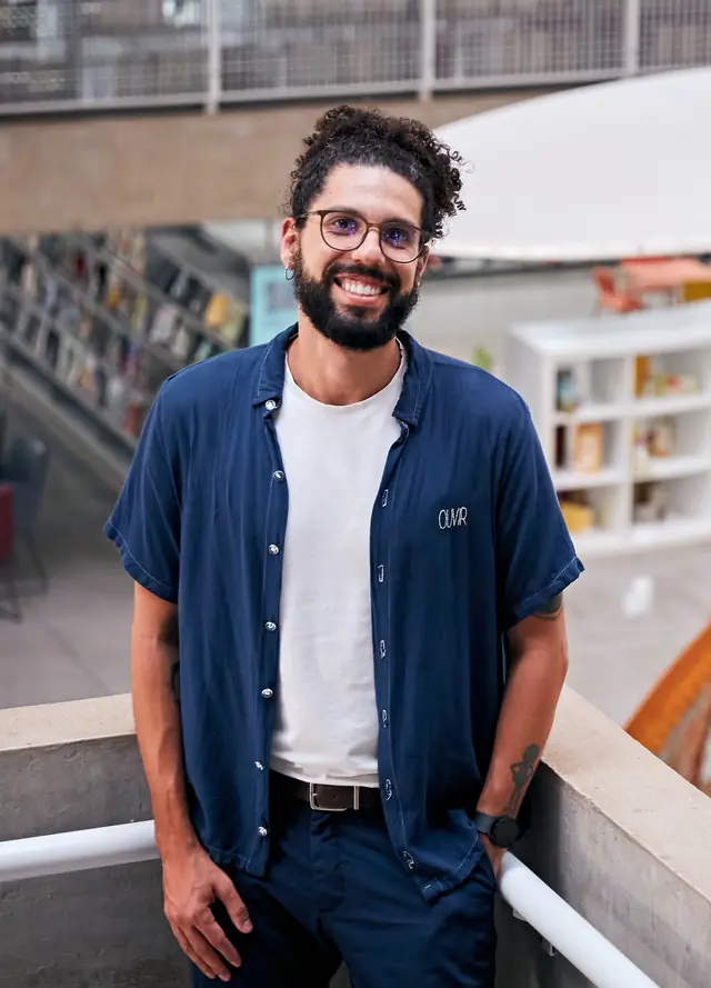 Retrato de João Victor Morais, psicólogo, sorrindo, apoiado em um corrimão